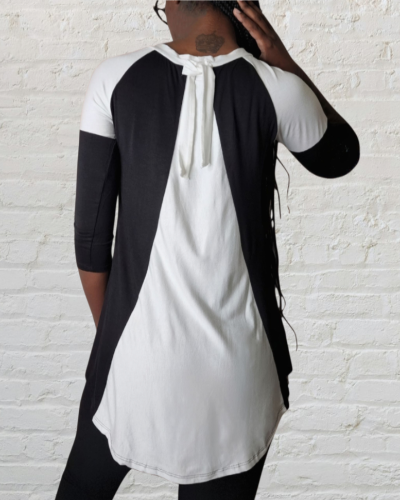Person wearing a black and white three-quarter sleeve shirt against a light brick wall.