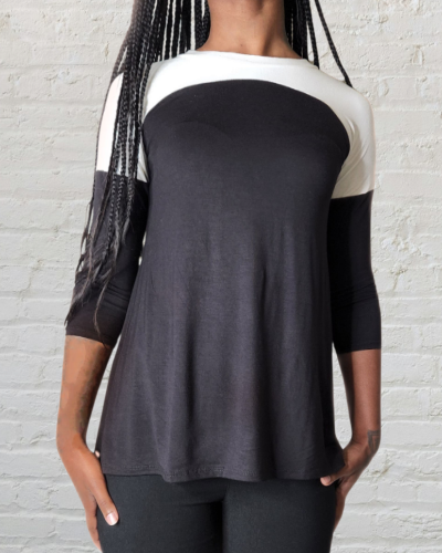 Person wearing a black and white three-quarter sleeve top against a light brick wall.