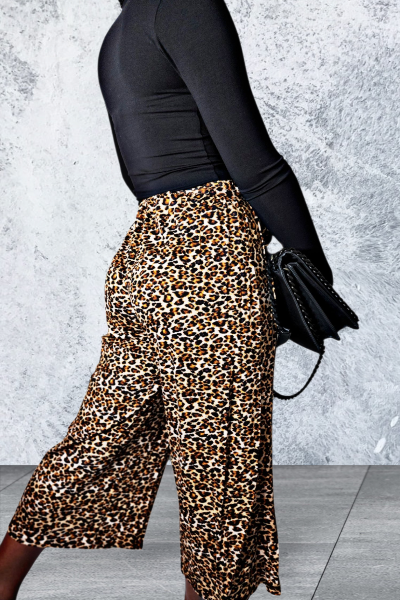 Person wearing leopard print pants and a black top against a gray concrete wall.