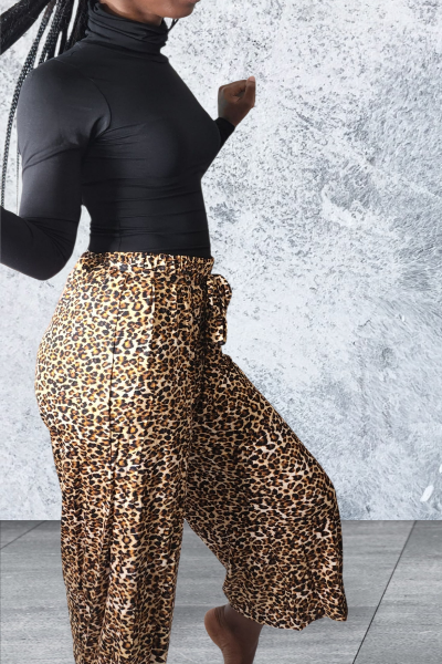 Person wearing a black top and leopard print pants against a textured gray wall.