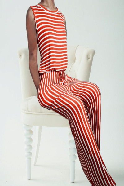 Person wearing a red and white striped jumpsuit sitting on a white chair against a white background