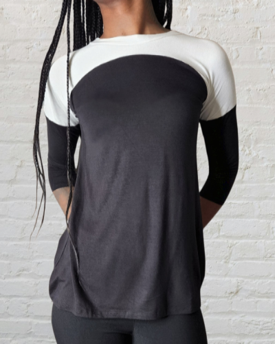 Person wearing a black and white three-quarter sleeve shirt against a light brick wall.