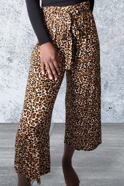 Person wearing leopard print pants against a gray concrete wall.