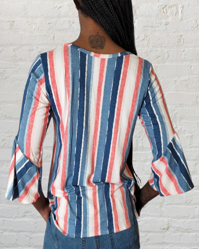 Person wearing a striped shirt with bell sleeves against a white brick wall.