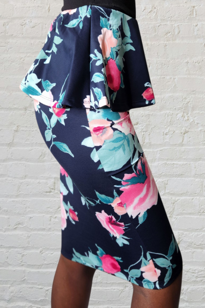 Floral skirt with pink and green flowers on a navy background against a white brick wall.