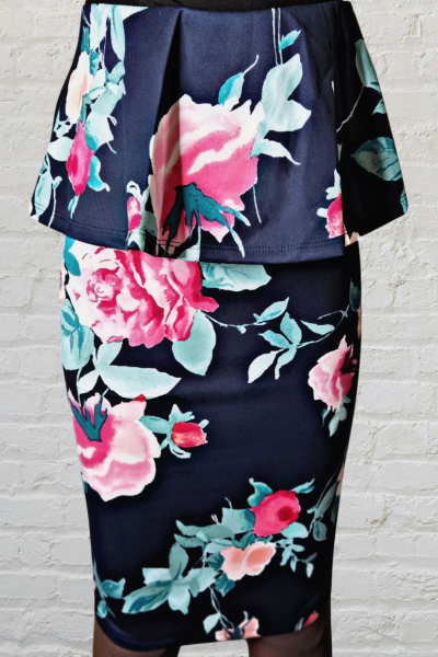 Floral skirt with pink and green flowers on a navy background against a white brick wall.
