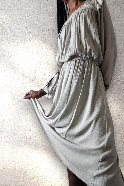 Person wearing a light, green-colored dress against a plain white wall